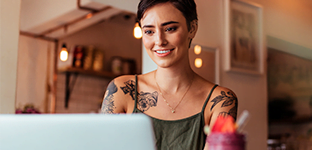 Mulher branca, com cabelo curto e tatuagens, mexendo no notebook.