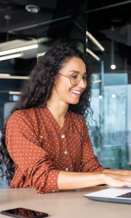 Mulher parda, com cabelo solto, usando óculos e mexendo no notebook.