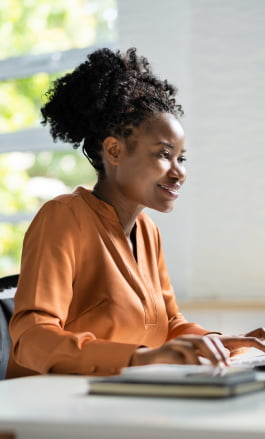 Mulher negra, com cabelo preso, olhando para a tela do computador.